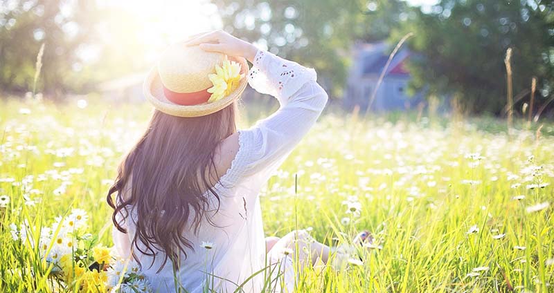 Frau mit Hut im Sonnenschein auf grüner Wiese